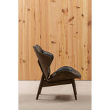 Stylish black leather effect chair featuring a curved design and plush cushioning, set against a backdrop of vertical wooden paneling.