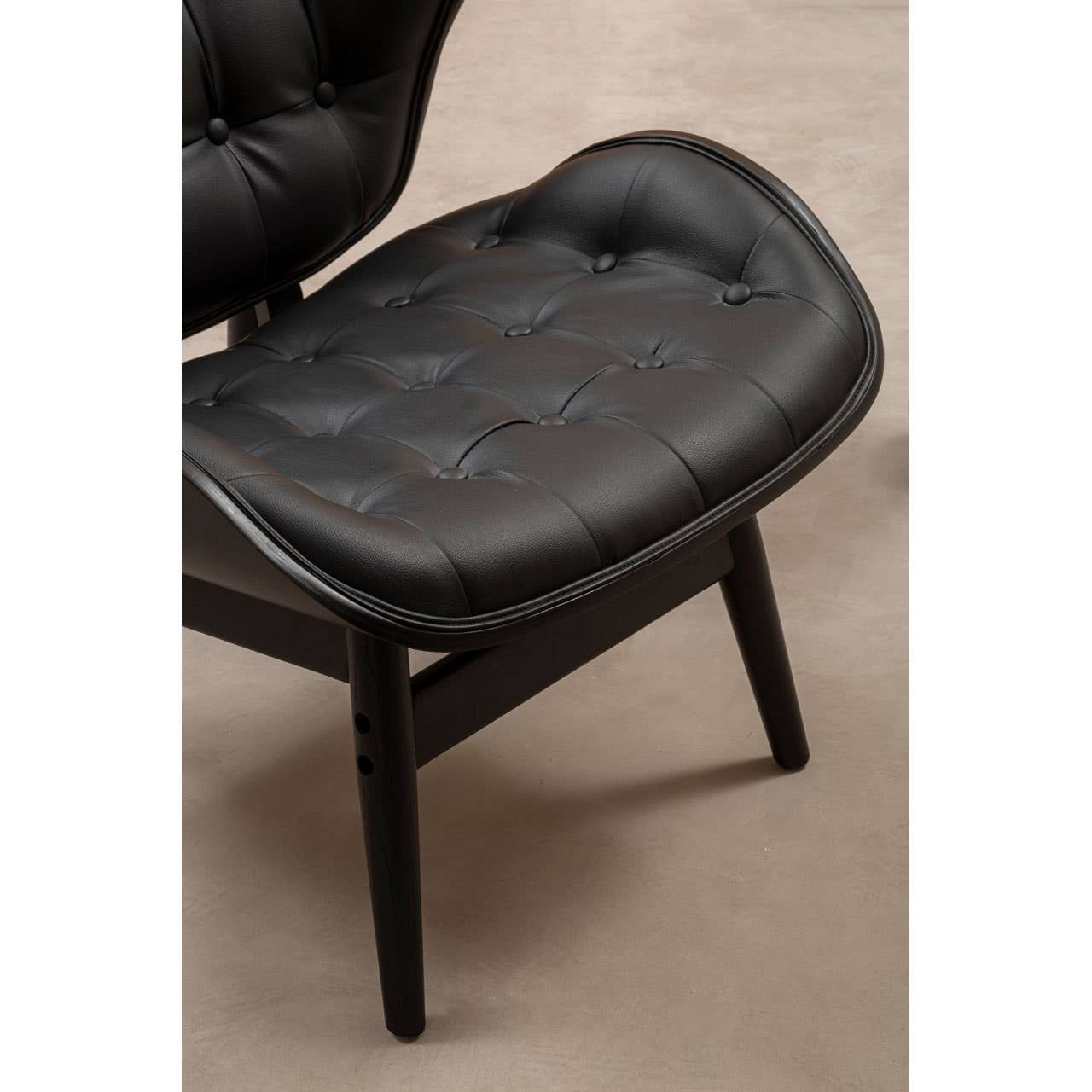 Black leather effect chair featuring a tufted seat and backrest, elegantly curved edges, and sturdy wooden legs.