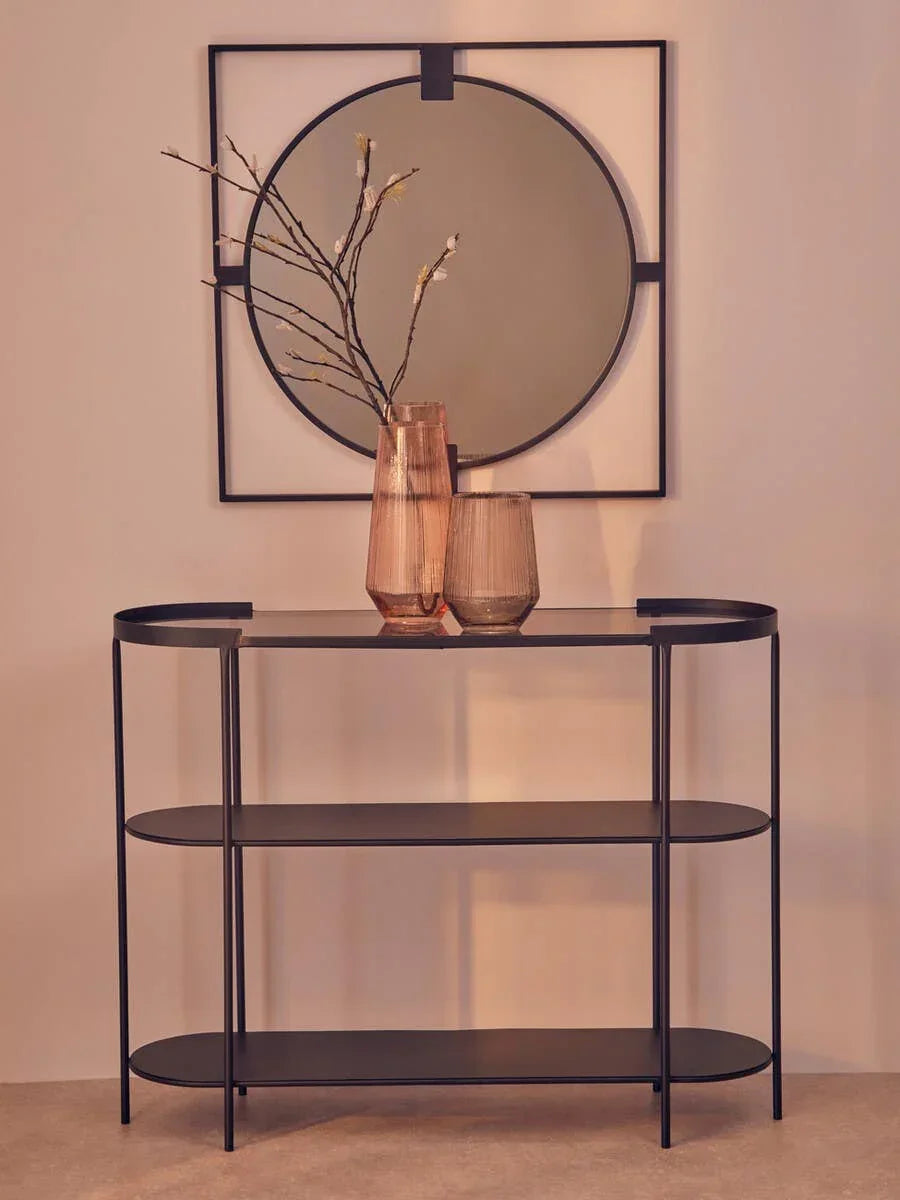 Black metal console table with glass vases and decorative branches, round wall mirror above