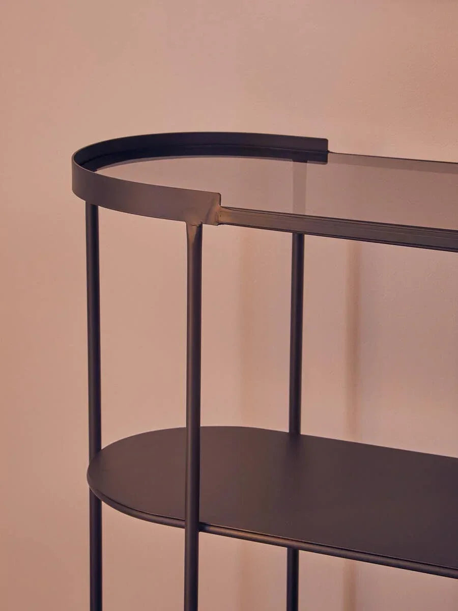 Black metal console table with glass top and lower shelf against a neutral wall