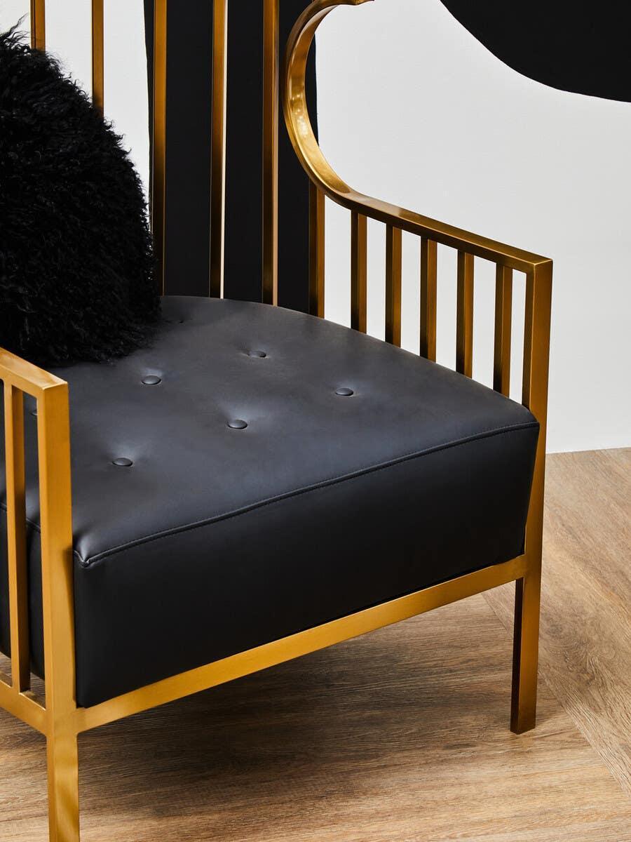 Black leather armchair with gold metal frame and tufted seat on wood floor