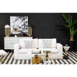 A cream fabric sofa with three seats, featuring decorative cushions, is positioned in a stylish living room setting. The backdrop includes a black wall adorned with abstract artwork, while a striped rug lies beneath the sofa. A modern side table and a decorative plant are also visible, adding to the contemporary decor
