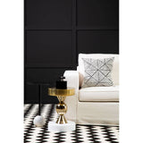 Cream fabric sofa with three seats, positioned next to a small gold and white side table. A decorative pillow with a geometric pattern rests on the sofa. The background features a black wall with a textured design, and the floor is covered with a black and white patterned rug