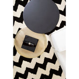 A cream fabric sofa with three seats, featuring soft cushions and a sleek design, positioned on a patterned black and white rug. A round black side table with a small decorative box sits nearby, enhancing the modern aesthetic of the space