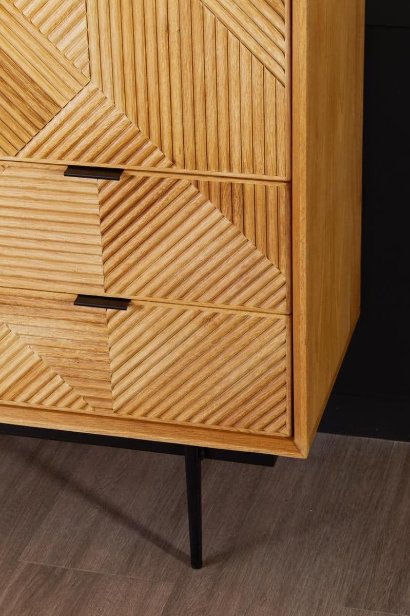 Natural finish cabinet featuring a textured geometric design on the front, two drawers with sleek black handles, and slender black legs. The cabinet is set against a dark background, highlighting its warm wood tones and intricate patterns