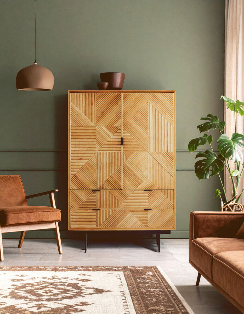 Natural finish cabinet with two doors and drawers, featuring a textured wood design, positioned against a green wall. A stylish brown armchair and a cozy sofa are visible in the foreground, along with a decorative rug. A potted plant adds a touch of greenery to the scene, and a pendant light hangs above the cabinet