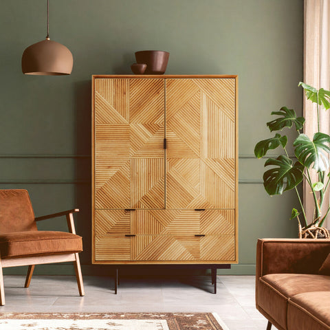 Natural finish cabinet with a geometric design, featuring two doors and four drawers, set against a green wall. A brown armchair and a potted plant are visible in the foreground, along with a pendant light hanging from the ceiling