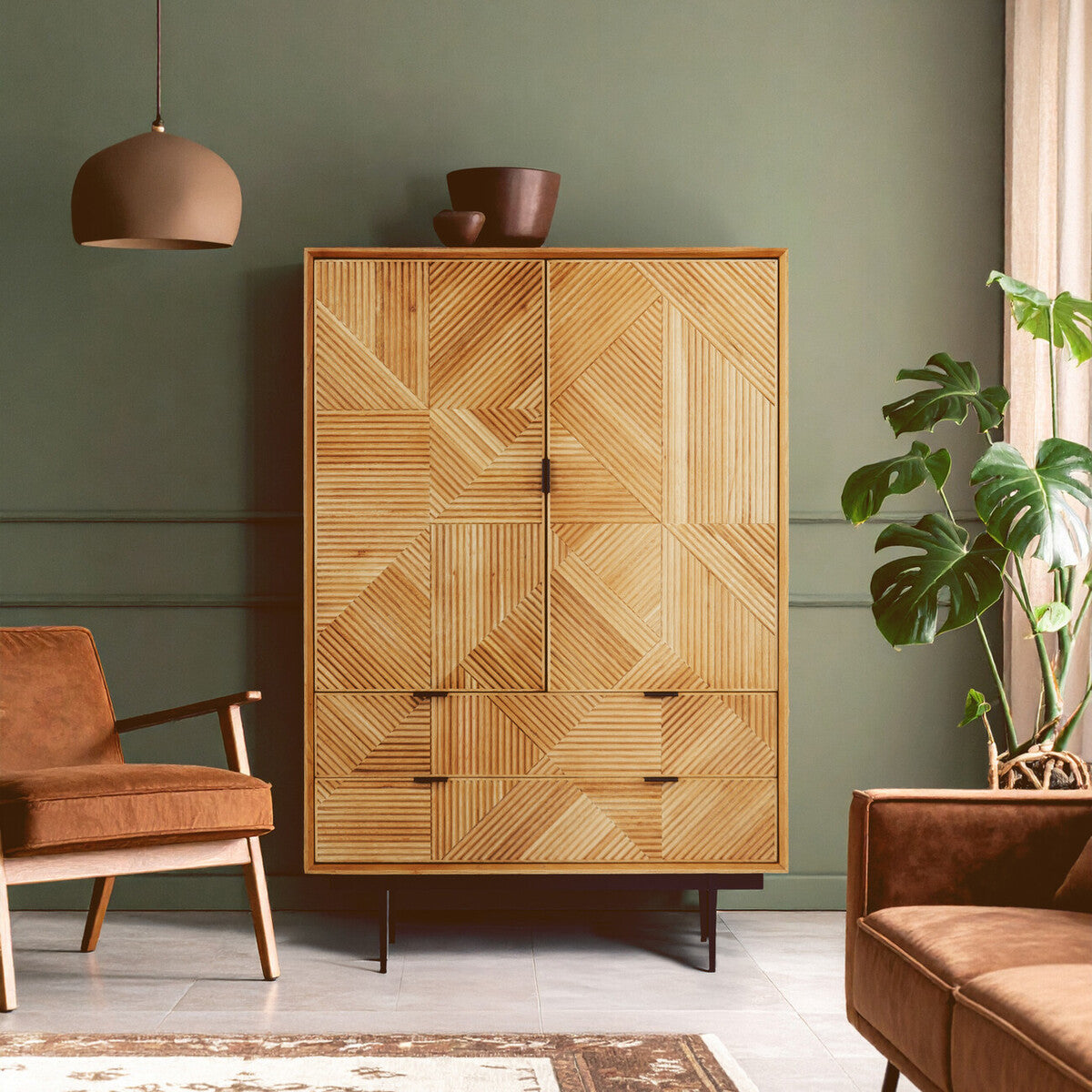 Natural finish cabinet with a geometric design, featuring two doors and four drawers, set against a green wall. A brown armchair and a potted plant are visible in the foreground, along with a pendant light hanging from the ceiling
