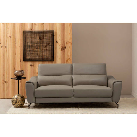 A three-seat sofa upholstered in stone-colored leather, featuring adjustable headrests and sleek armrests. The sofa is positioned in a modern living space with a light wooden wall in the background and a decorative wall art piece. A small round side table with a decorative bowl sits beside the sofa, enhancing the contemporary aesthetic