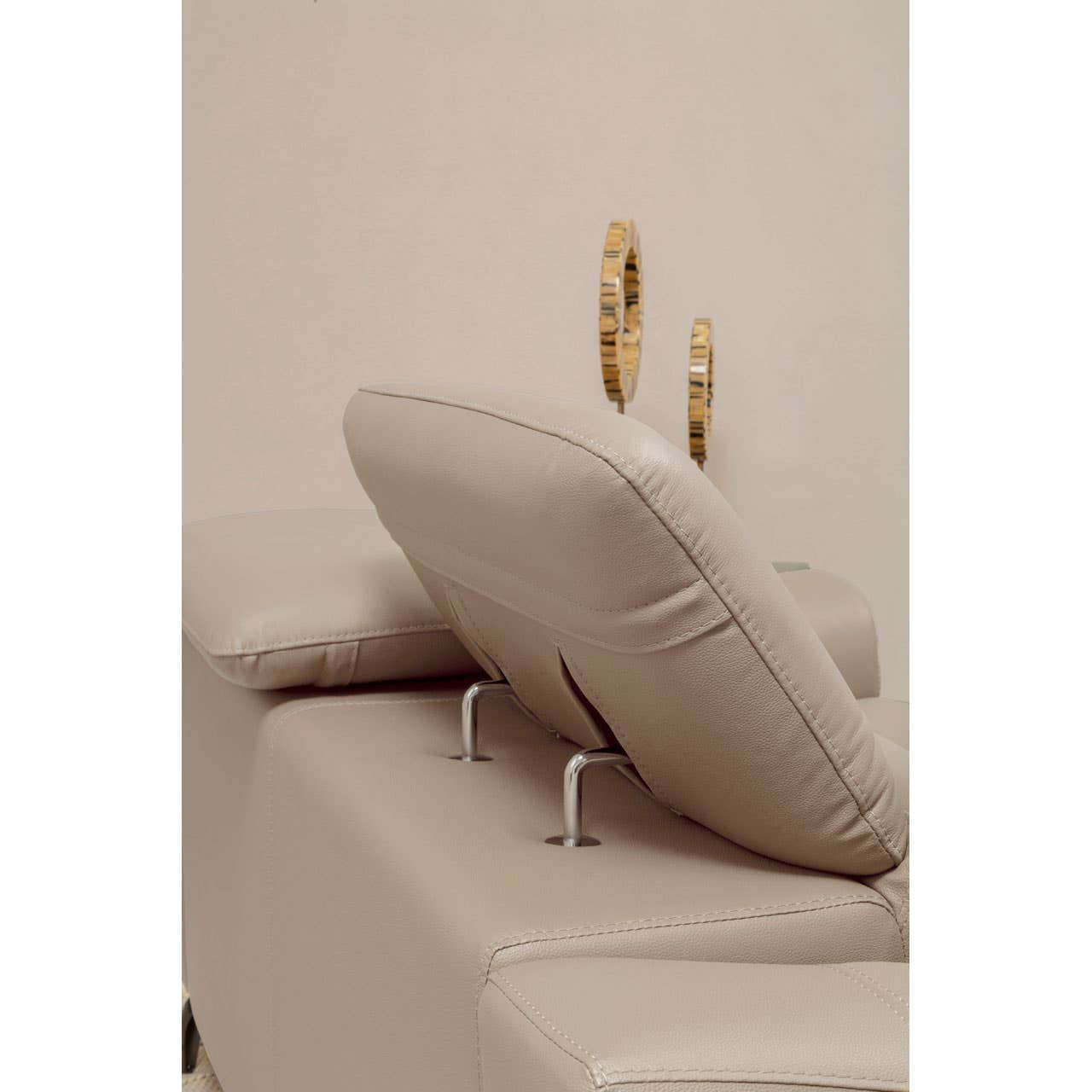 A close-up view of a stone leather sofa featuring adjustable headrests, showcasing the soft, plush texture of the upholstery and the sleek metal supports for the headrests. The background is a neutral color, enhancing the sofa's elegant design