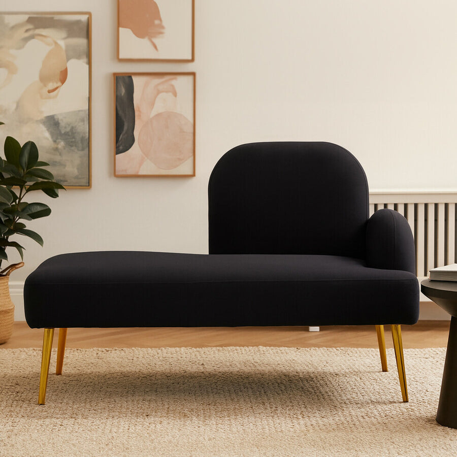 A sleek black chaise longue with a right-hand armrest, featuring a modern design and wooden legs. The chaise is positioned on a light-colored rug, with abstract wall art and a potted plant in the background, creating a stylish living space ambiance