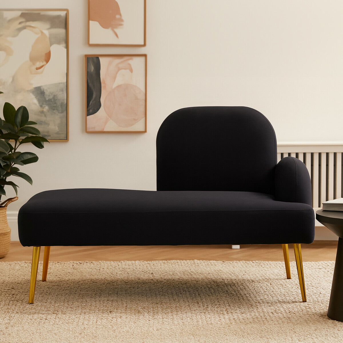 A sleek black chaise longue with a rounded backrest and a small armrest on the right side, supported by elegant gold legs. The chaise is placed on a light-colored rug in a modern living space, with abstract artwork and a plant visible in the background