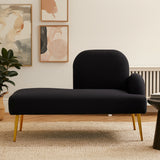 A sleek black chaise longue with a rounded backrest and a small armrest on the right side, supported by elegant gold legs. The chaise is placed on a light-colored rug in a modern living space, with abstract artwork and a plant visible in the background