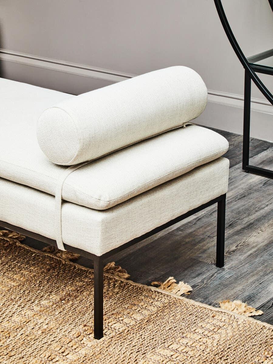 Cream upholstered daybed with black metal legs and bolster cushion on woven rug