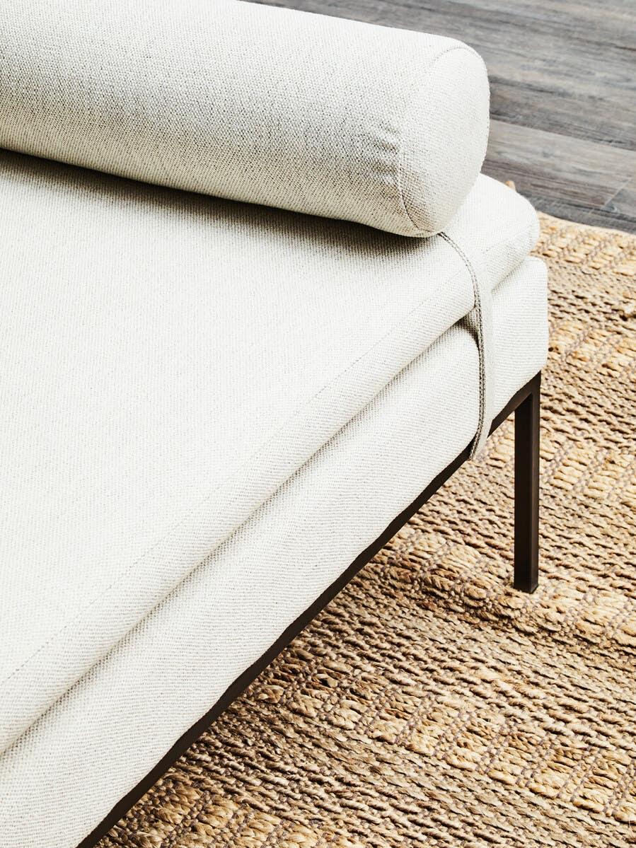 Cream fabric sofa with bolster cushion and black metal legs on woven rug