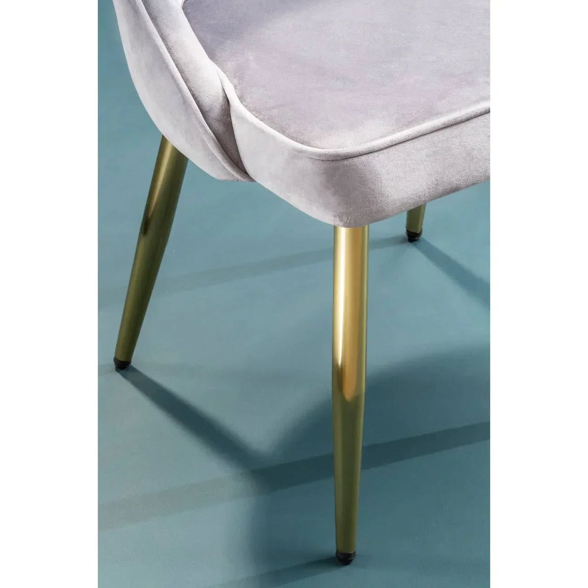 Grey velvet dining chair with gold metal legs on blue floor, close-up view