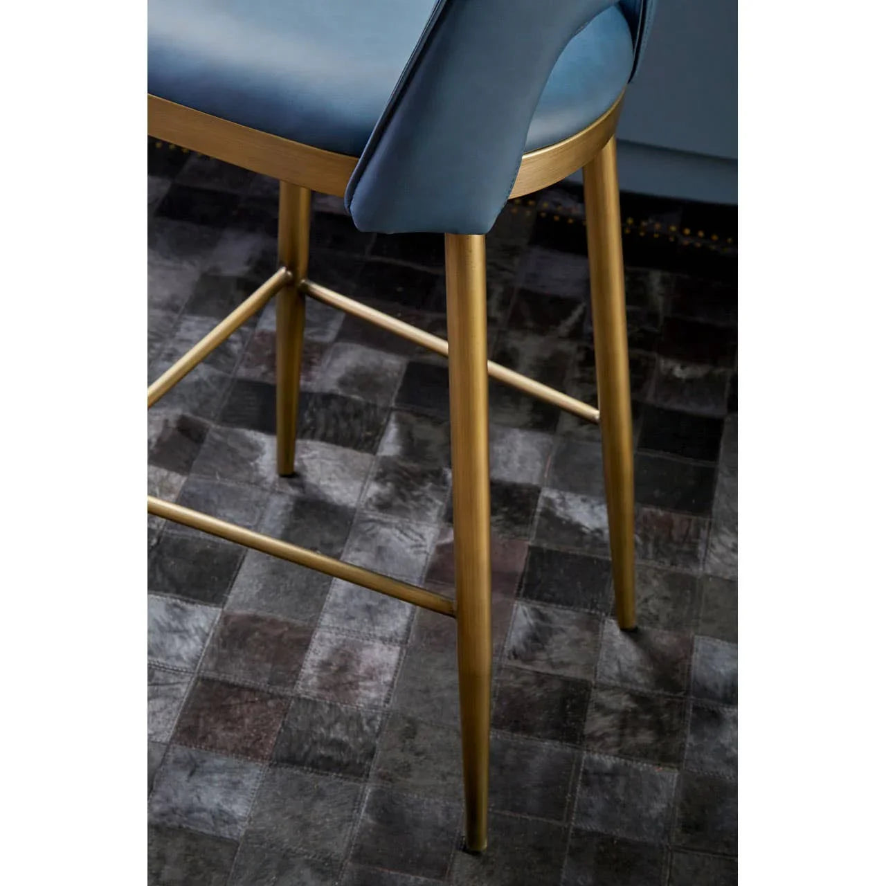 Blue upholstered bar stool with gold metal legs on dark tiled flooring