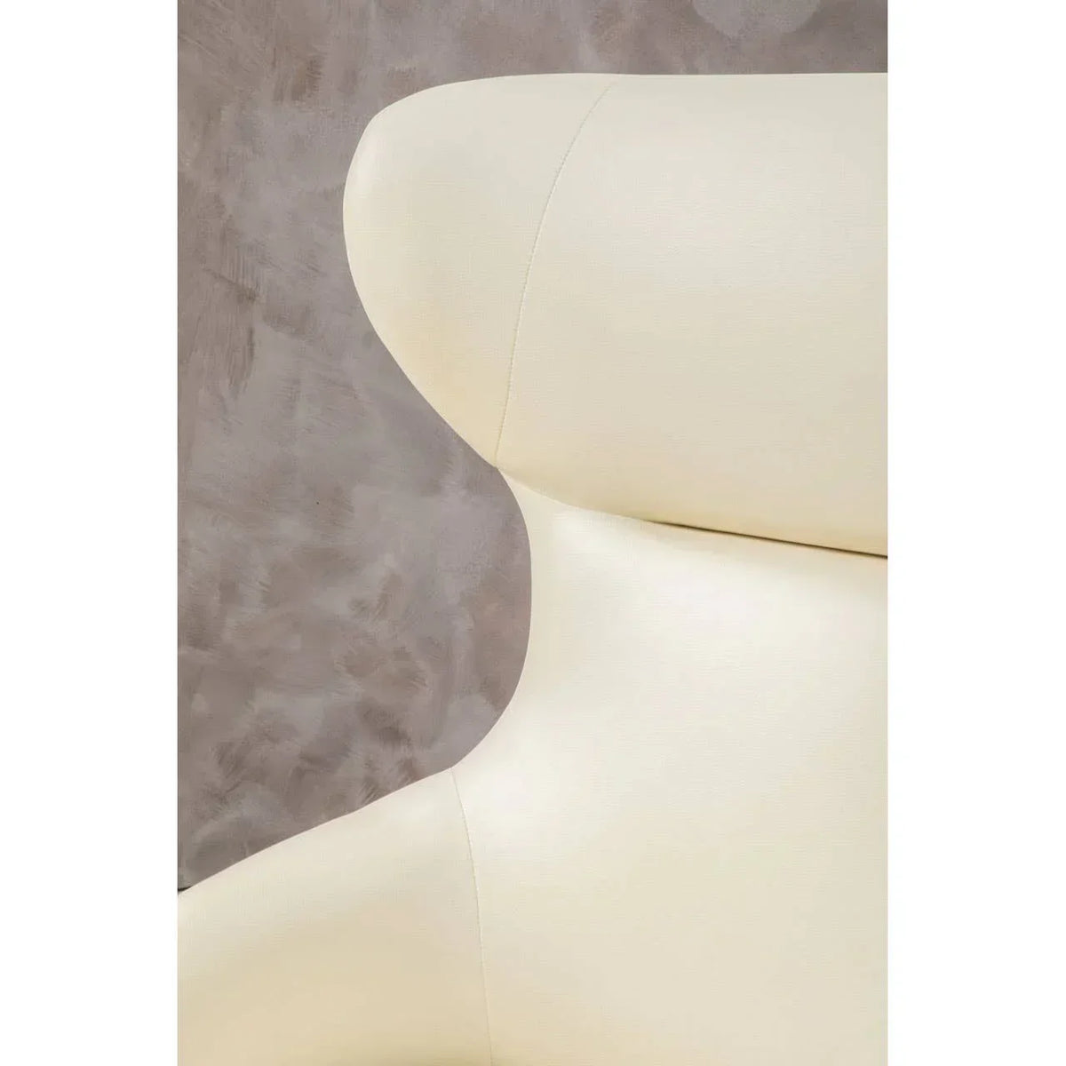 Close-up of cream leather armchair backrest against textured grey wall