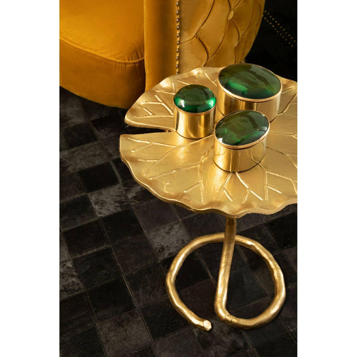 Gold leaf side table with decorative green glass jars beside mustard velvet armchair