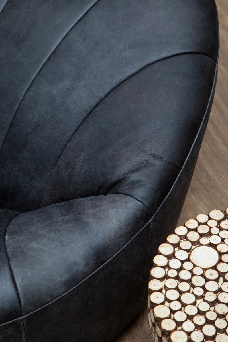Curved black leather armchair with stitched detail next to round wooden accent table