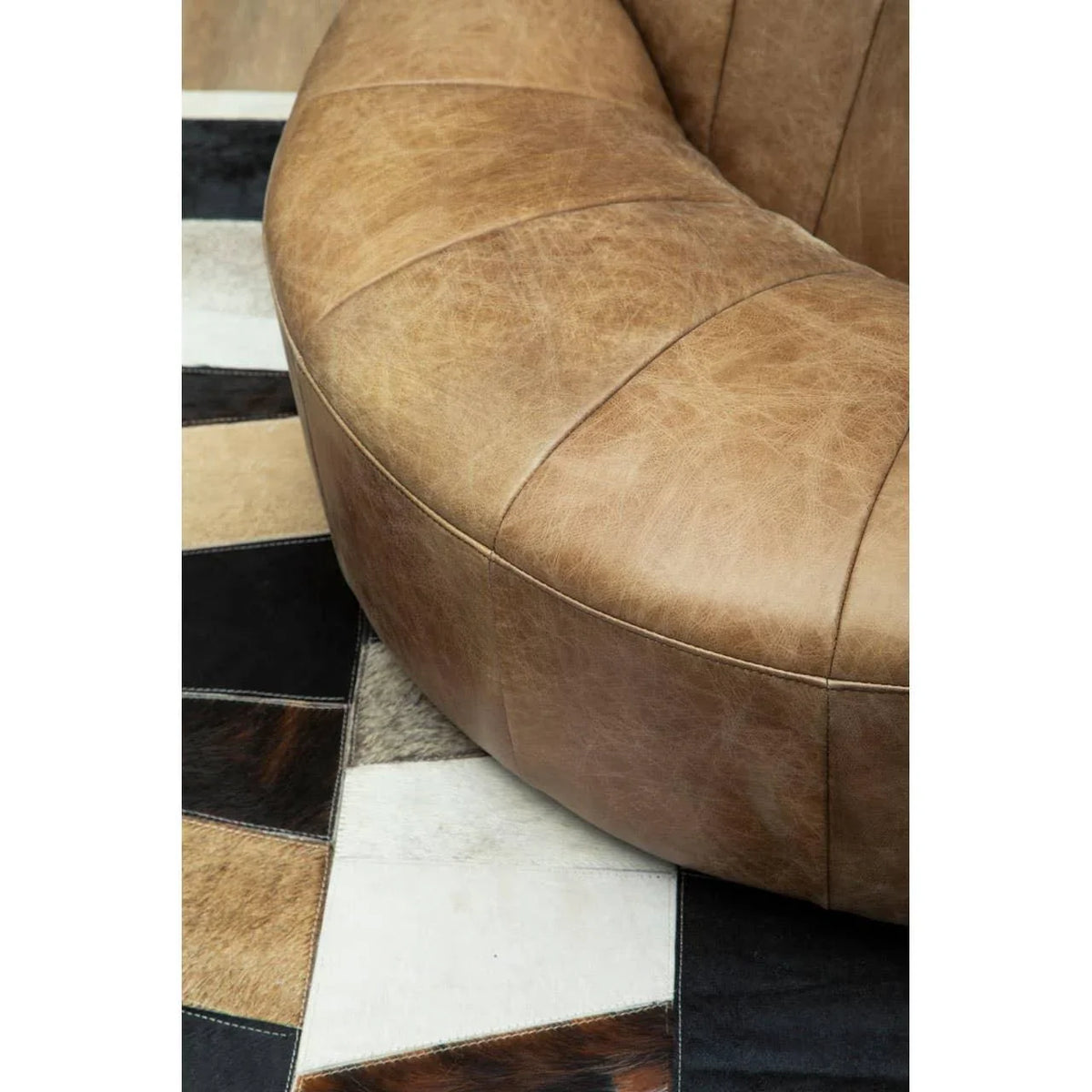 Tan leather sofa armrest close-up with patchwork cowhide rug beneath