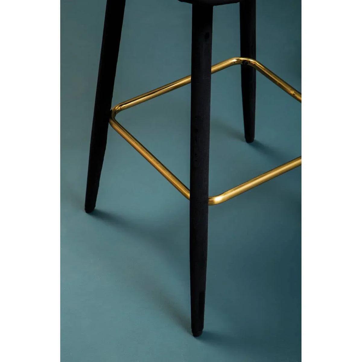 Black bar stool legs with gold metal footrest on teal floor