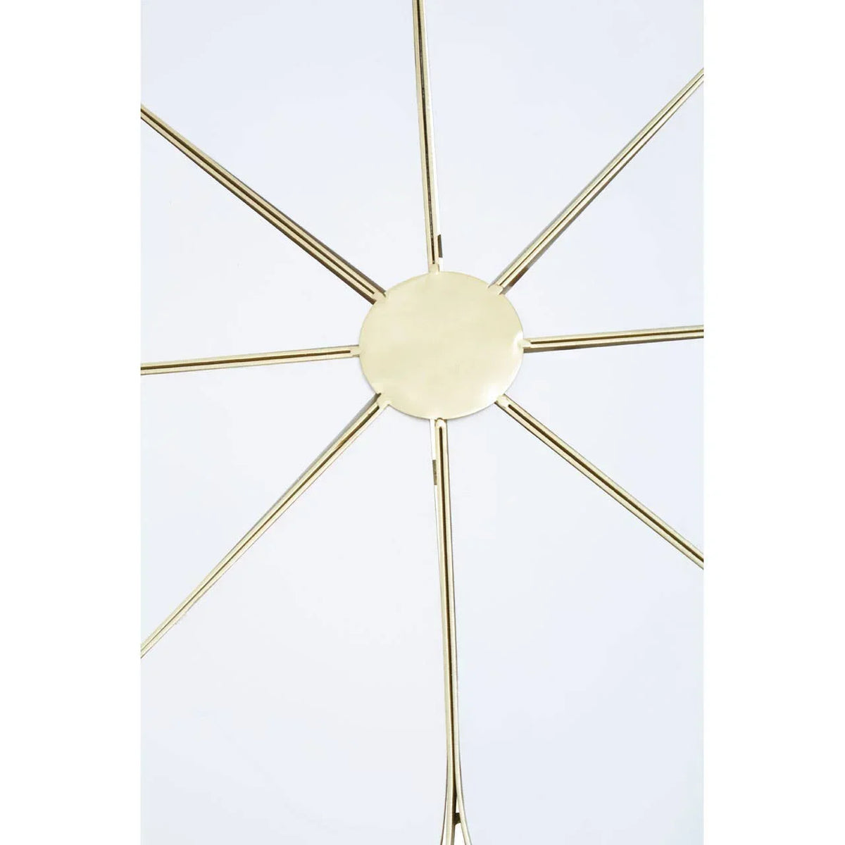 Gold metal wall art with radiating spokes and circular center on white background