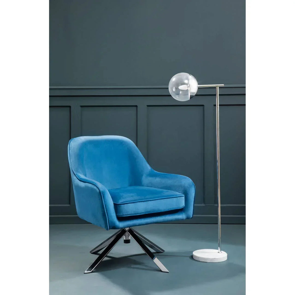 Blue velvet swivel accent chair with chrome base next to modern floor lamp against dark wall