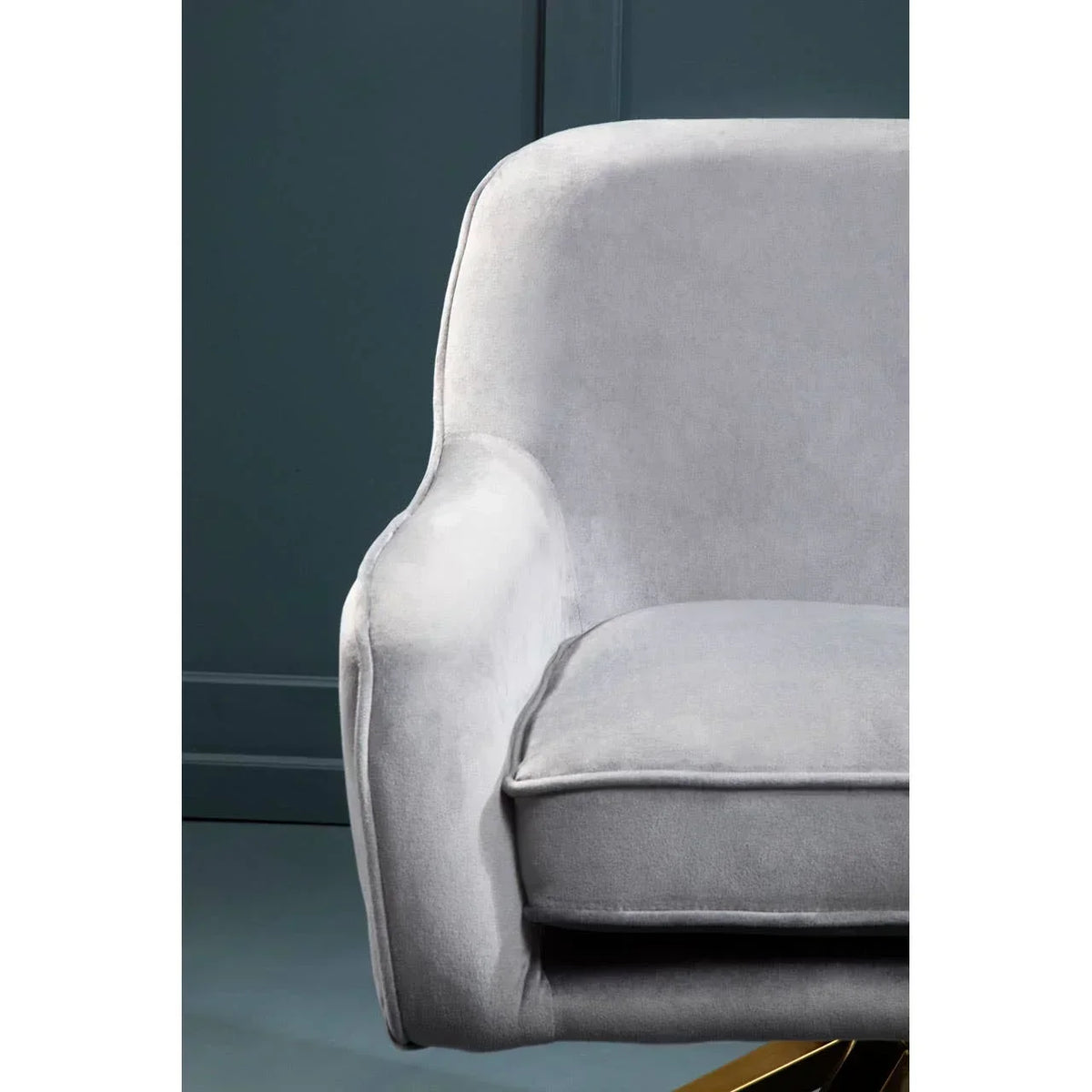 Light grey velvet armchair with curved armrest and cushioned seat against dark wall