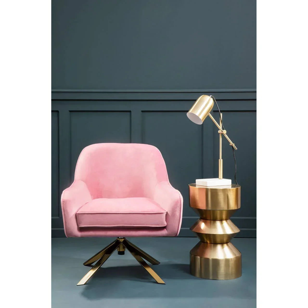 Pink velvet armchair with gold metal legs beside gold side table and modern desk lamp