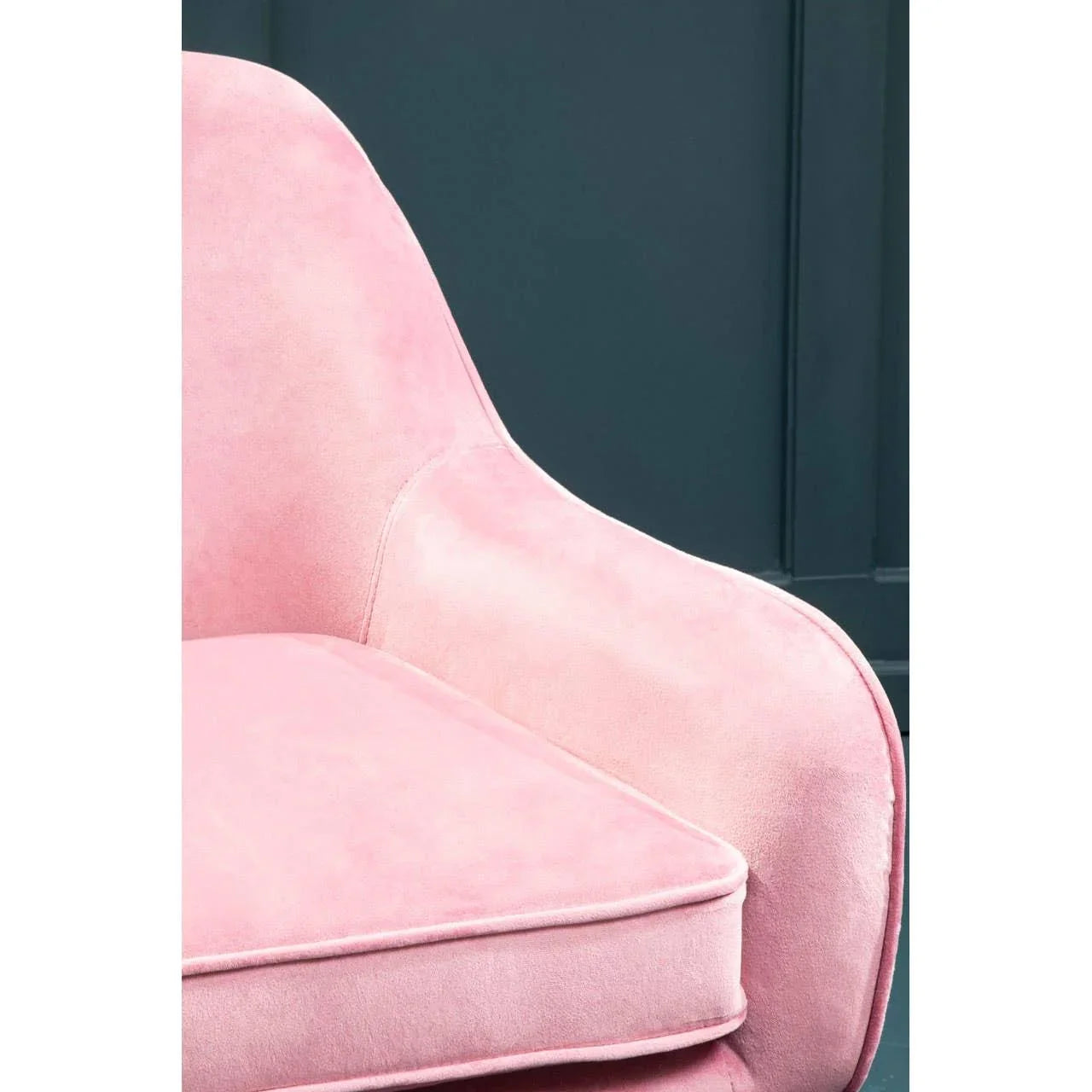 Close up of pink velvet armchair with curved armrest against dark panel wall