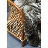 Natural rattan chair with a high backrest, featuring a woven design and a light wood finish, partially covered by a soft, textured gray throw blanket, set against a blue background