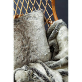 A high back chair made of natural rattan, featuring a woven design and a warm wooden frame. The chair is adorned with a plush, textured throw blanket and a decorative pillow, adding a cozy touch to the seating area. The background is a dark, contrasting color that highlights the chair's natural materials