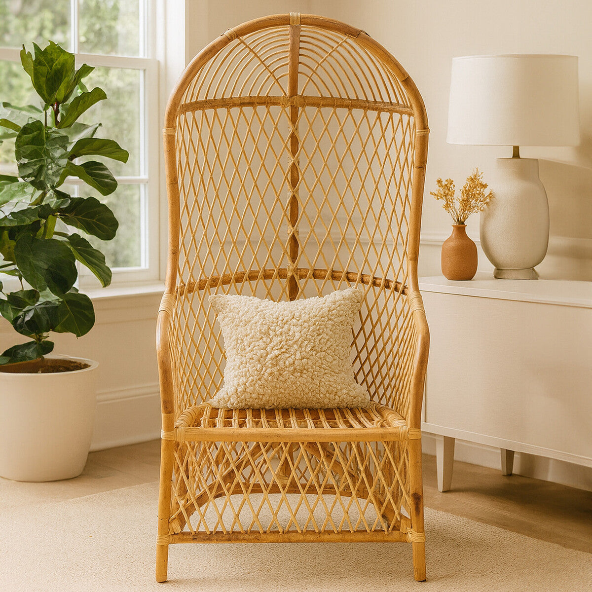 High back chair made of natural rattan with a woven design, featuring a comfortable seat and a decorative cushion. The chair is positioned in a bright room with a potted plant and a lamp in the background, creating a cozy atmosphere