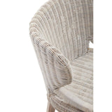 A close-up view of the Manado Wicker Chair showcasing its textured woven seat and backrest in a light, natural color, with a curved armrest and wooden legs