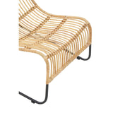 Close-up view of the Manado Rattan Chair showcasing its woven rattan seat and backrest, complemented by a sleek black metal frame. The design features a curved shape, emphasizing comfort and style, with a matching footstool visible in the background