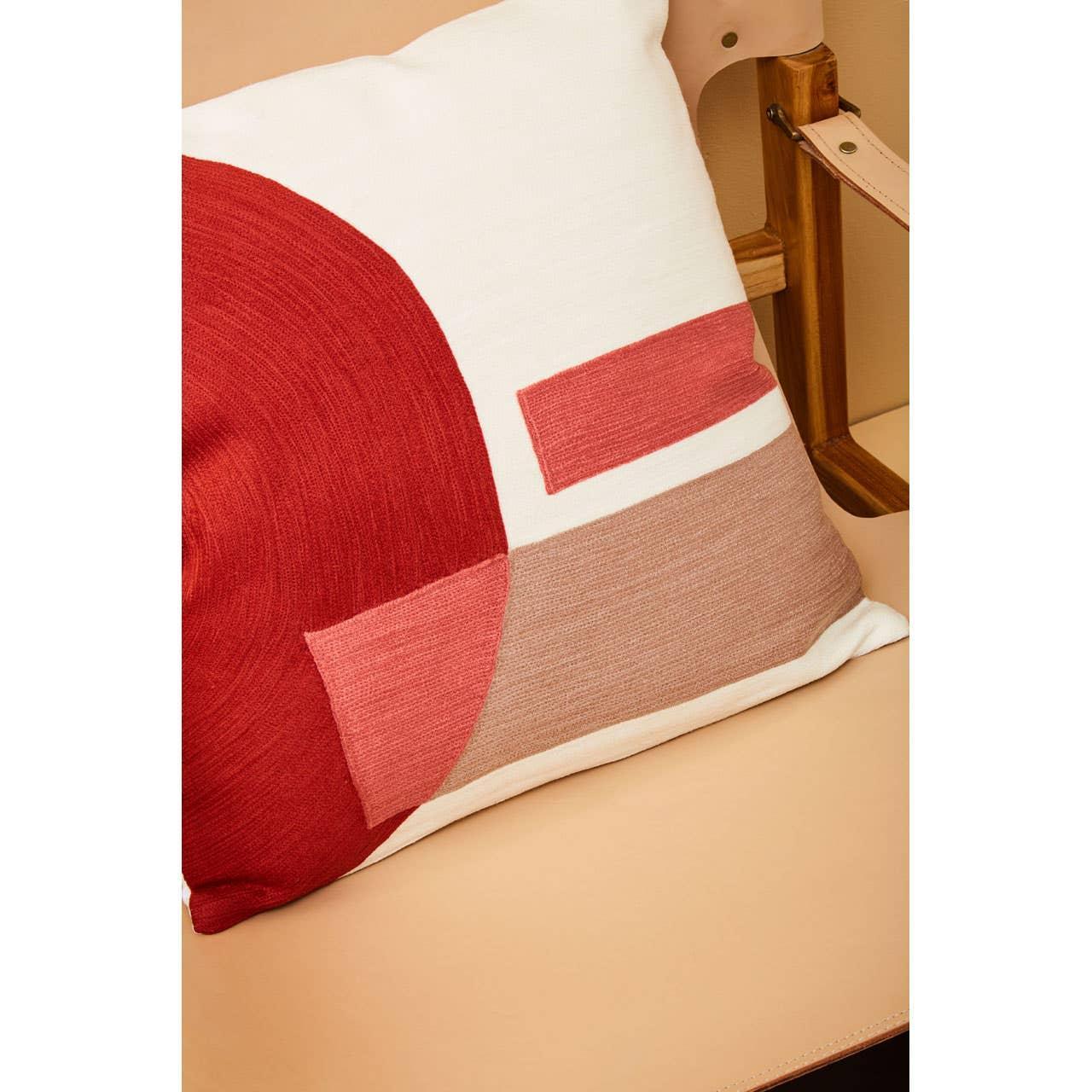 Geometric cushion with red, pink, and beige pattern on a light tan leather chair