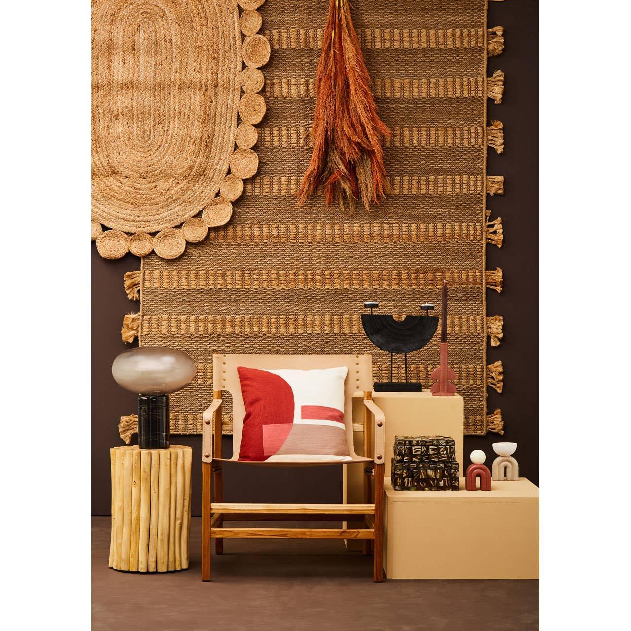 Wooden accent chair with red and white cushion, side table, and woven rug wall decor