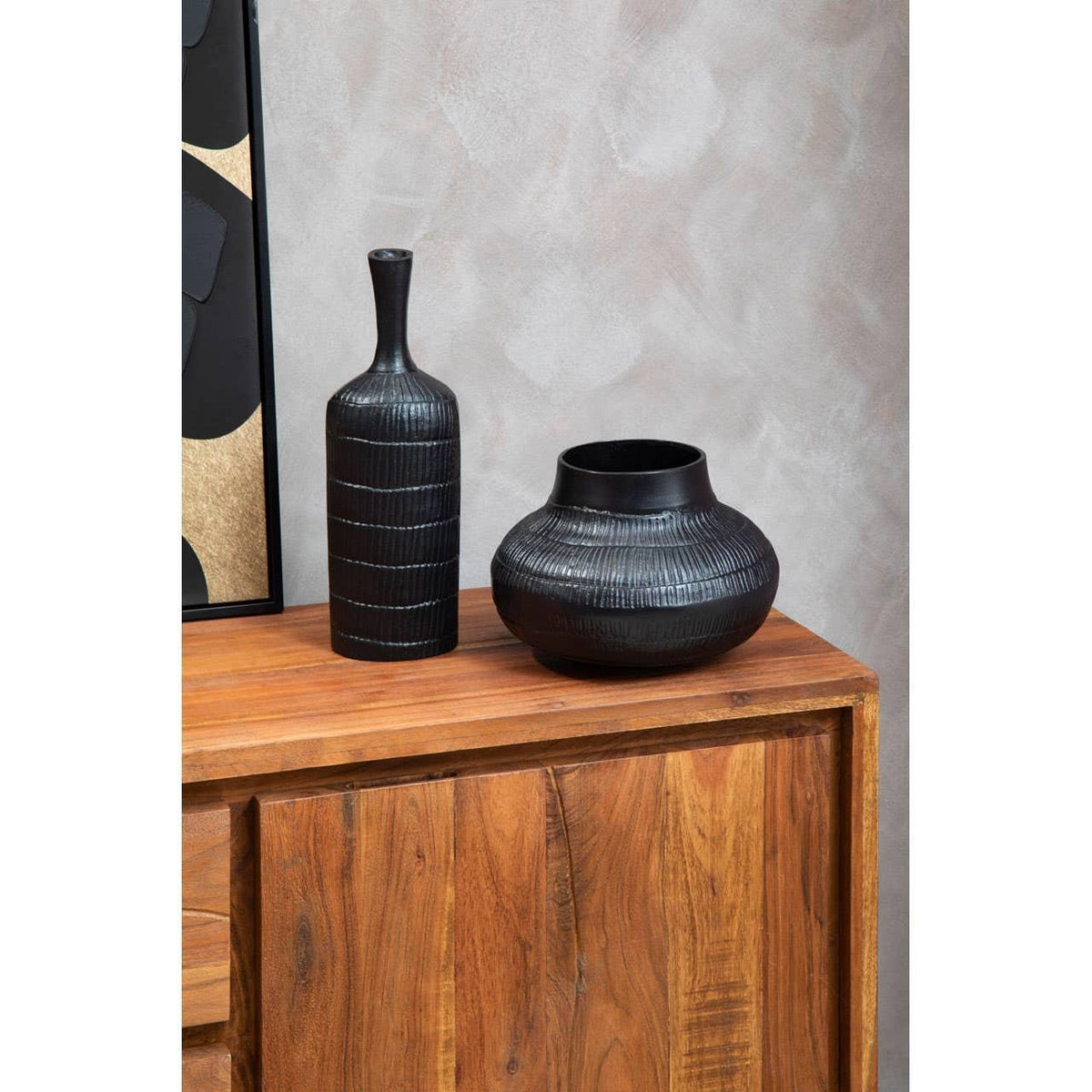 Black ceramic vase set on wooden sideboard against textured wall