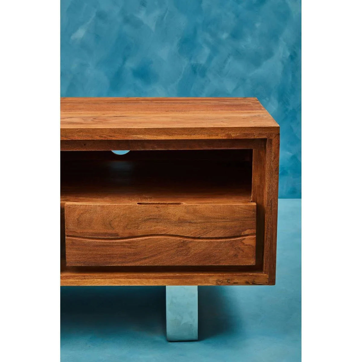 Solid wood TV unit with drawer, open shelf and metal leg against blue backdrop