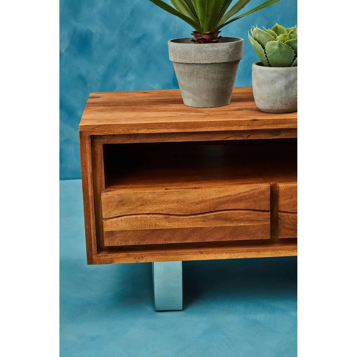 Wooden side table with metal legs, open shelf, potted plants on top, blue background