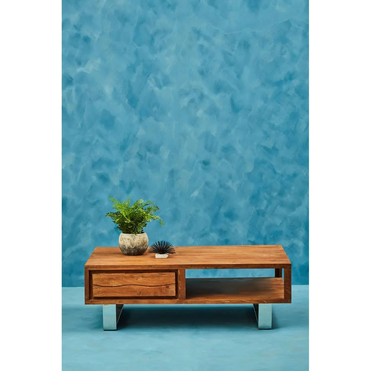 Rectangular wooden coffee table with drawer, silver legs, and plant decor on top