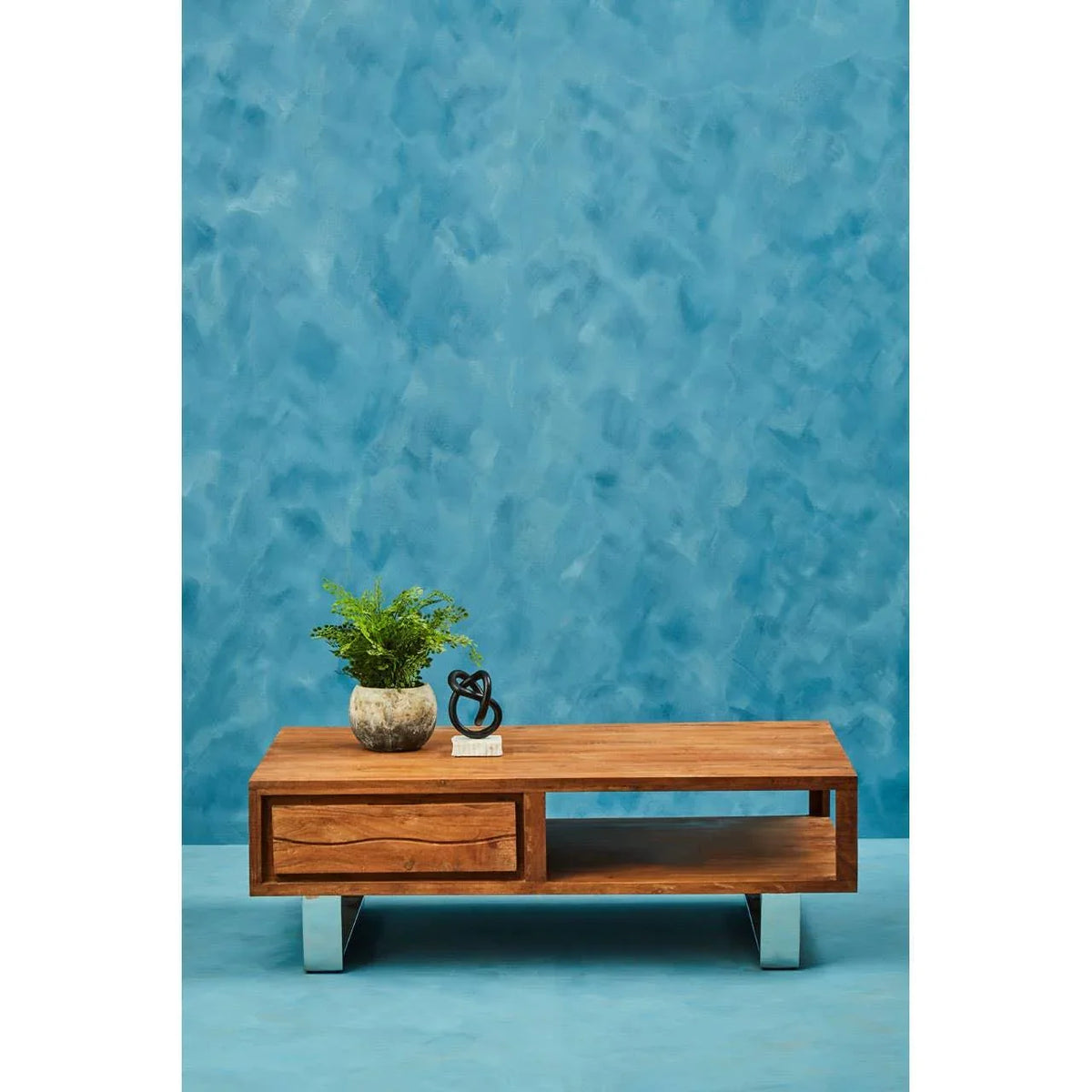 Wooden coffee table with drawer, chrome legs, and decor against blue wall