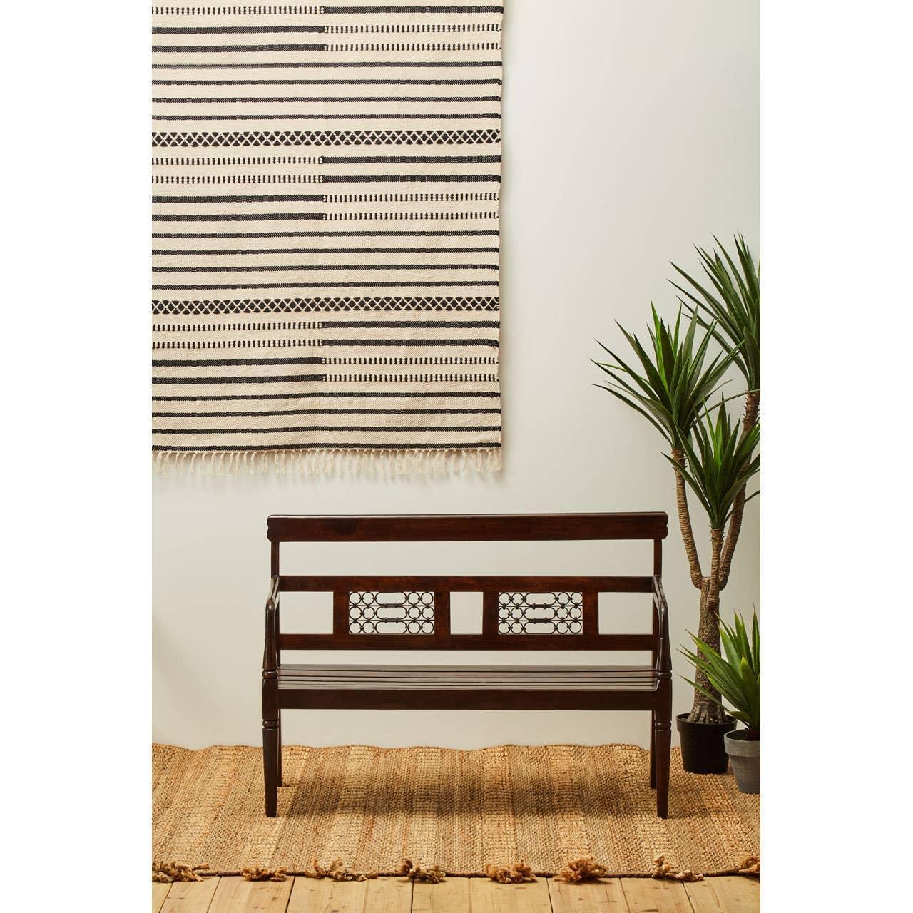 Dark wood bench with lattice backrest on a woven rug beside green indoor plants