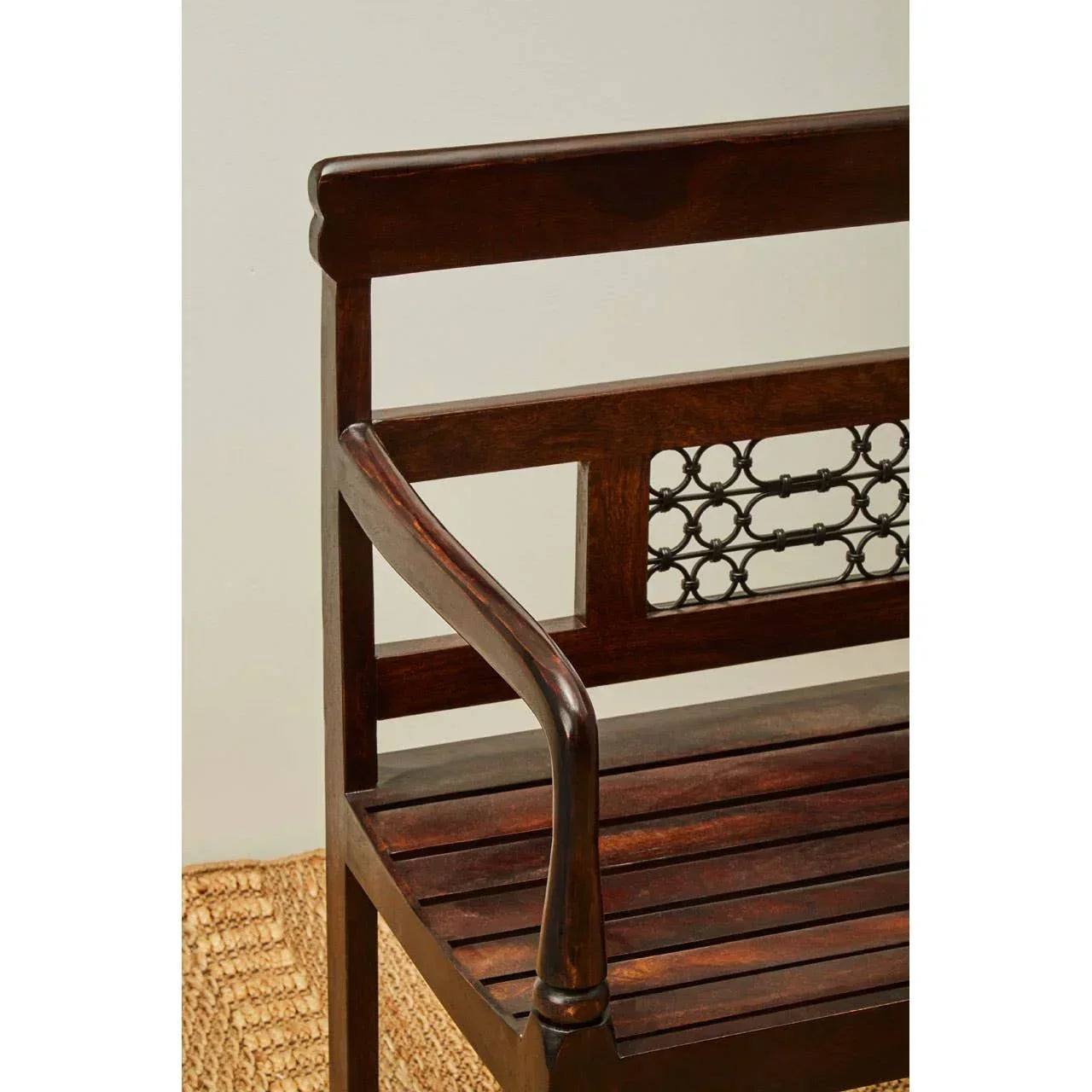 Dark wood bench with slatted seat and metal lattice backrest detail on woven rug