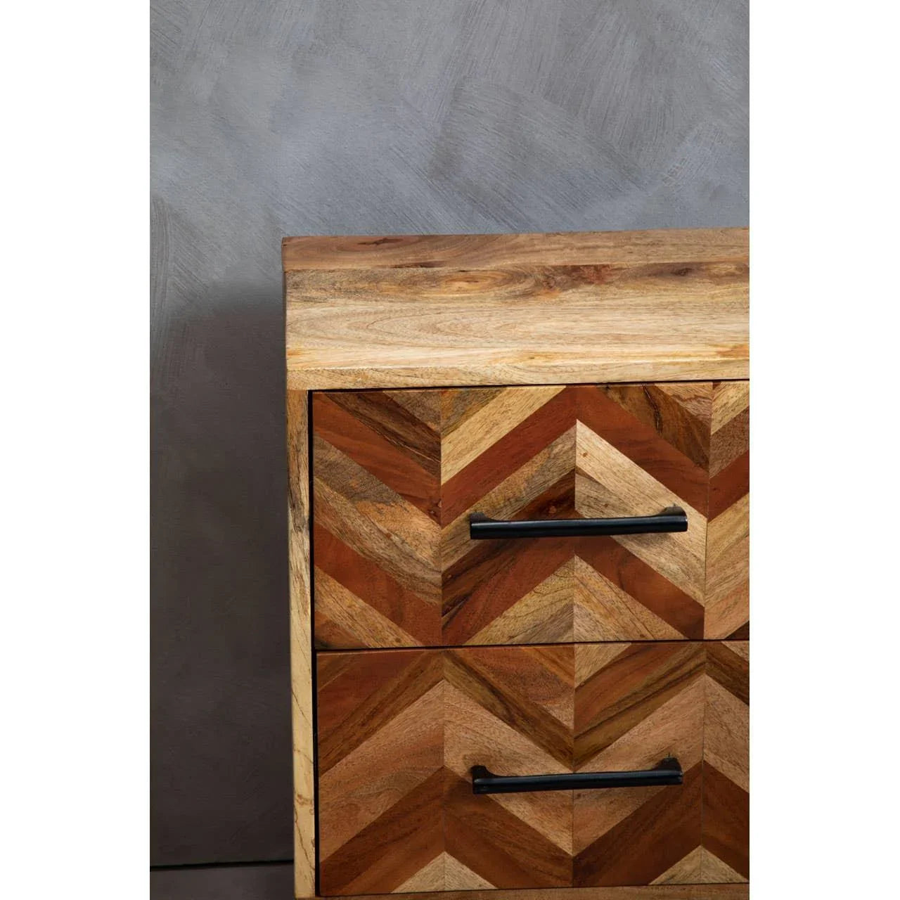 Chevron pattern wooden chest of drawers with black handles against grey wall