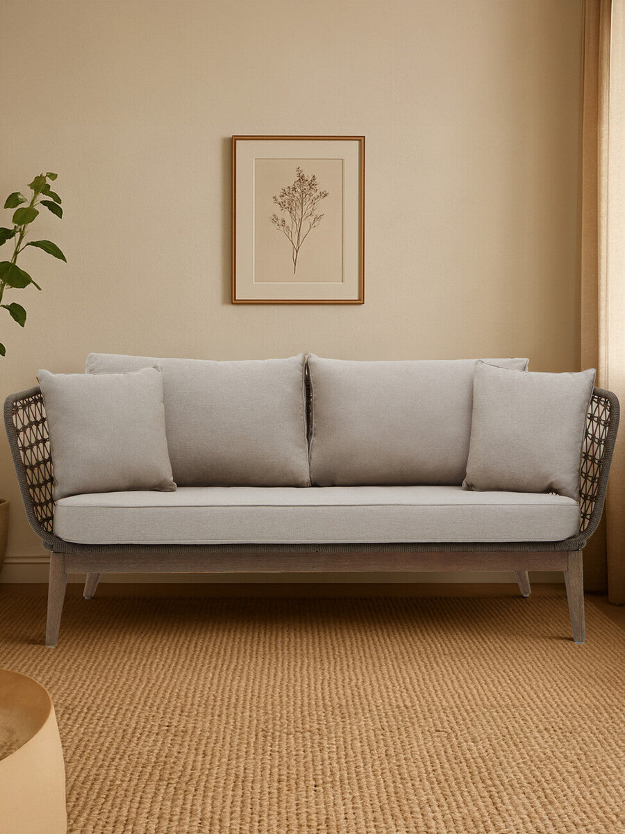 Three-seater sofa featuring a grey woven rope design with plush cushions in a cozy living space. The sofa is positioned against a light-colored wall, complemented by a decorative wall art piece and a potted plant nearby. The flooring is a warm, neutral tone, enhancing the inviting atmosphere