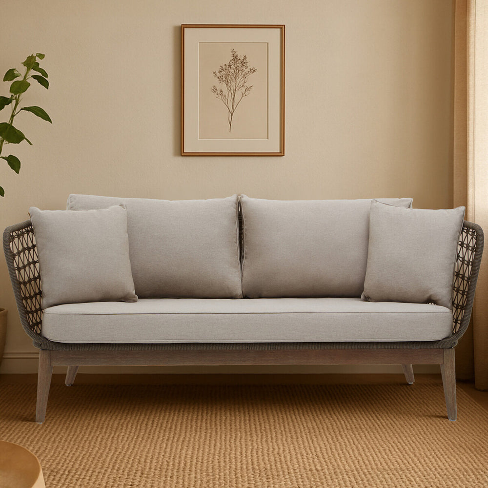 Three-seater sofa featuring a grey woven rope design with a sturdy frame, complemented by plush light grey cushions. The sofa is positioned against a neutral-colored wall, with a framed botanical print above it and a potted plant to the side, set on a warm-toned carpet
