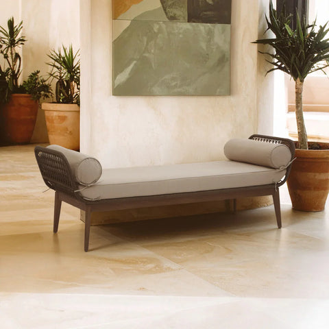 Modern daybed with taupe cushion and bolster pillows in indoor space with potted plants