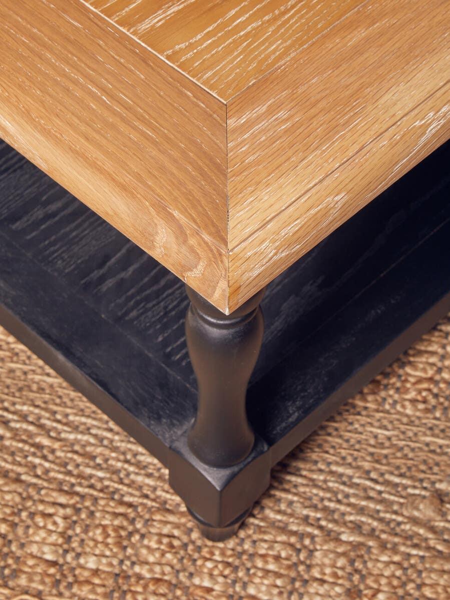 Oak coffee table corner with black turned leg and lower shelf on woven rug